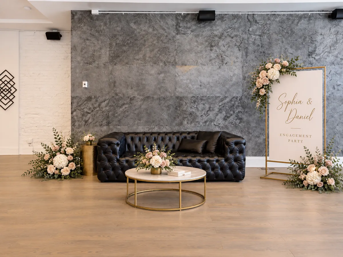 Engagement party setup at 3535 Venue: the black leather sofa by the stone accent wall with blush and white flowers, a marble coffee table and a welcome sign (virtually staged)