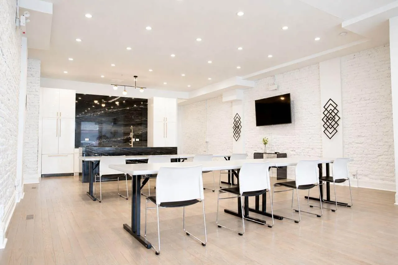 Main room at 3535 Venue set with long white tables and chairs in front of the black marble kitchen