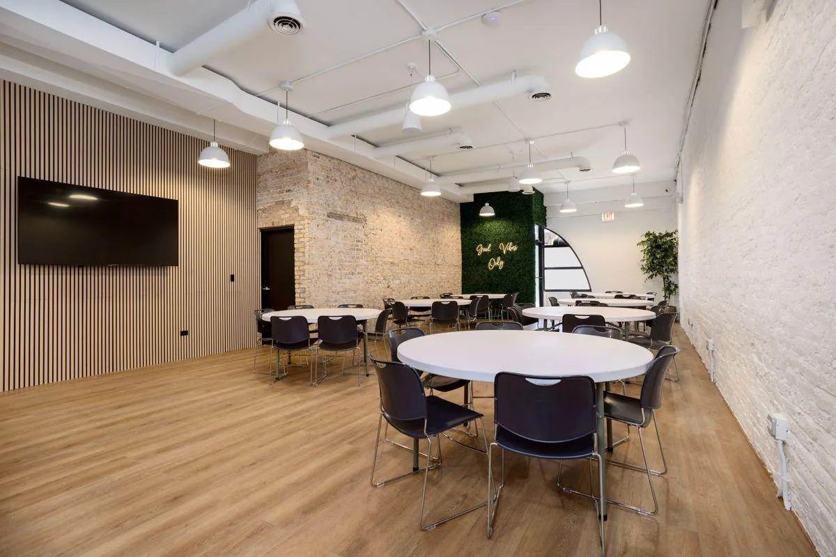 Montrose Studio main room set with round tables, a wall-mounted TV and exposed brick