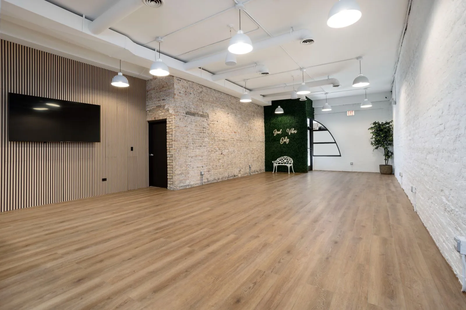 Montrose Studio open main room with a wood slat wall, wall-mounted TV, and exposed brick