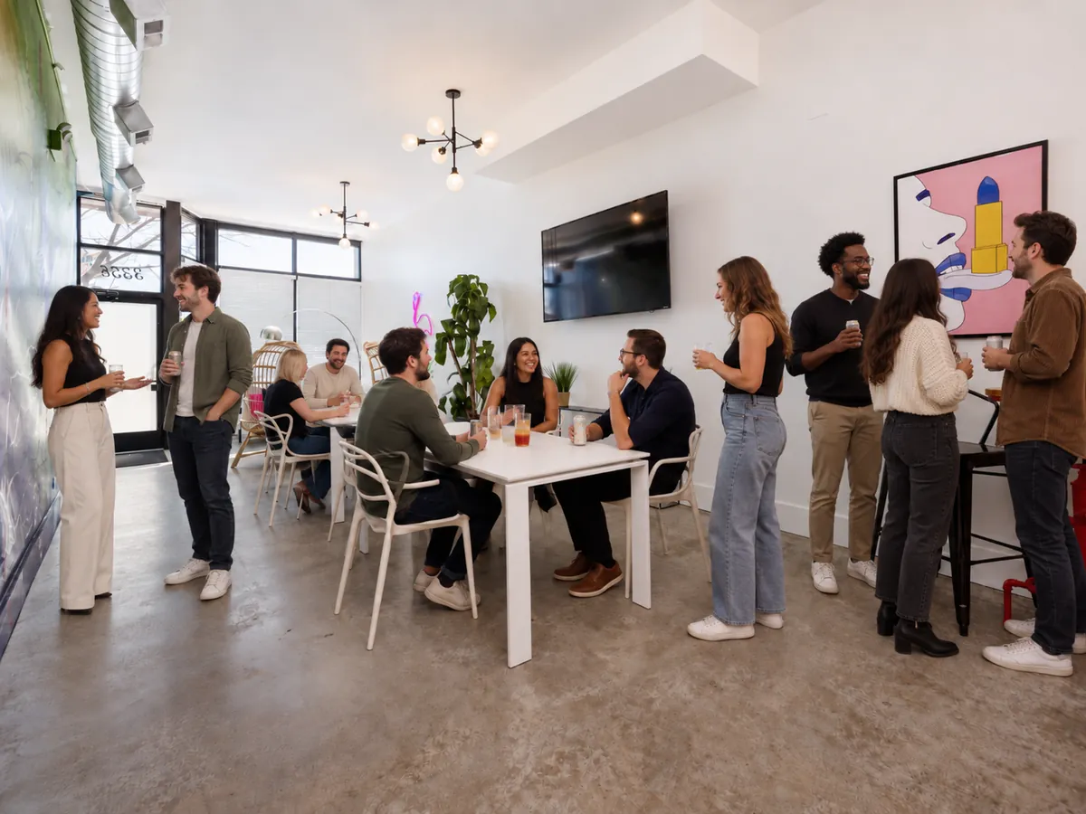 Party at Nala’s Party Room: guests mingling with drinks around the white tables, by the TV and the pop-art print (virtually staged)
