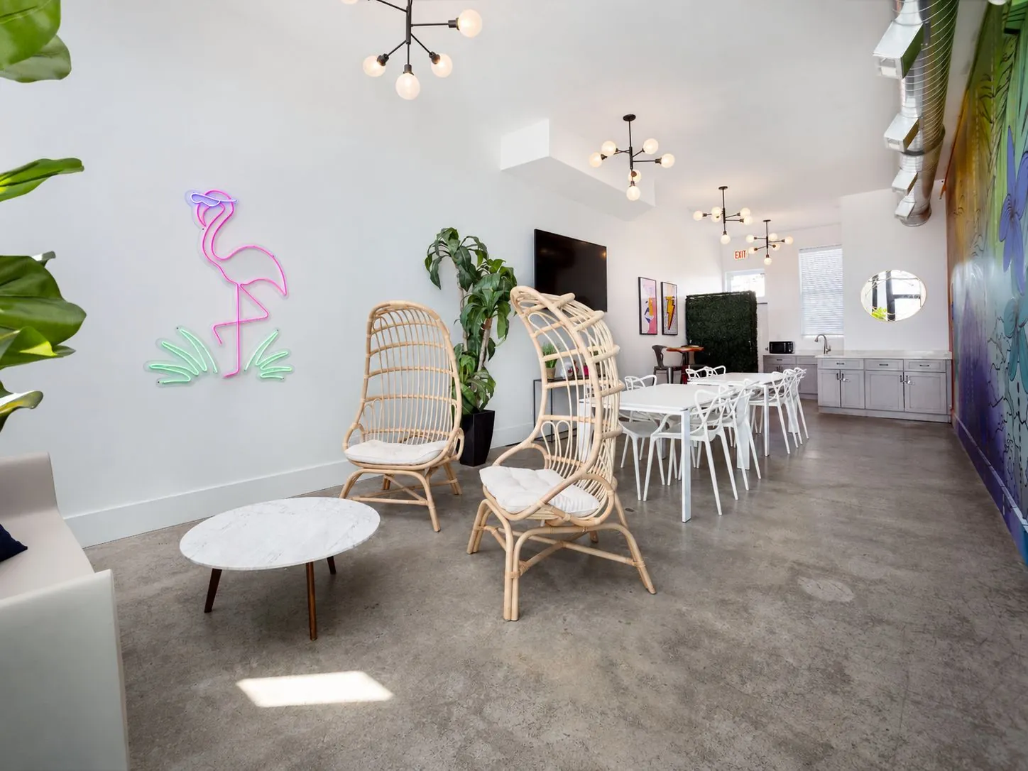 Lounge area with rattan egg chairs, a marble coffee table, and a neon flamingo sign, with dining tables beyond