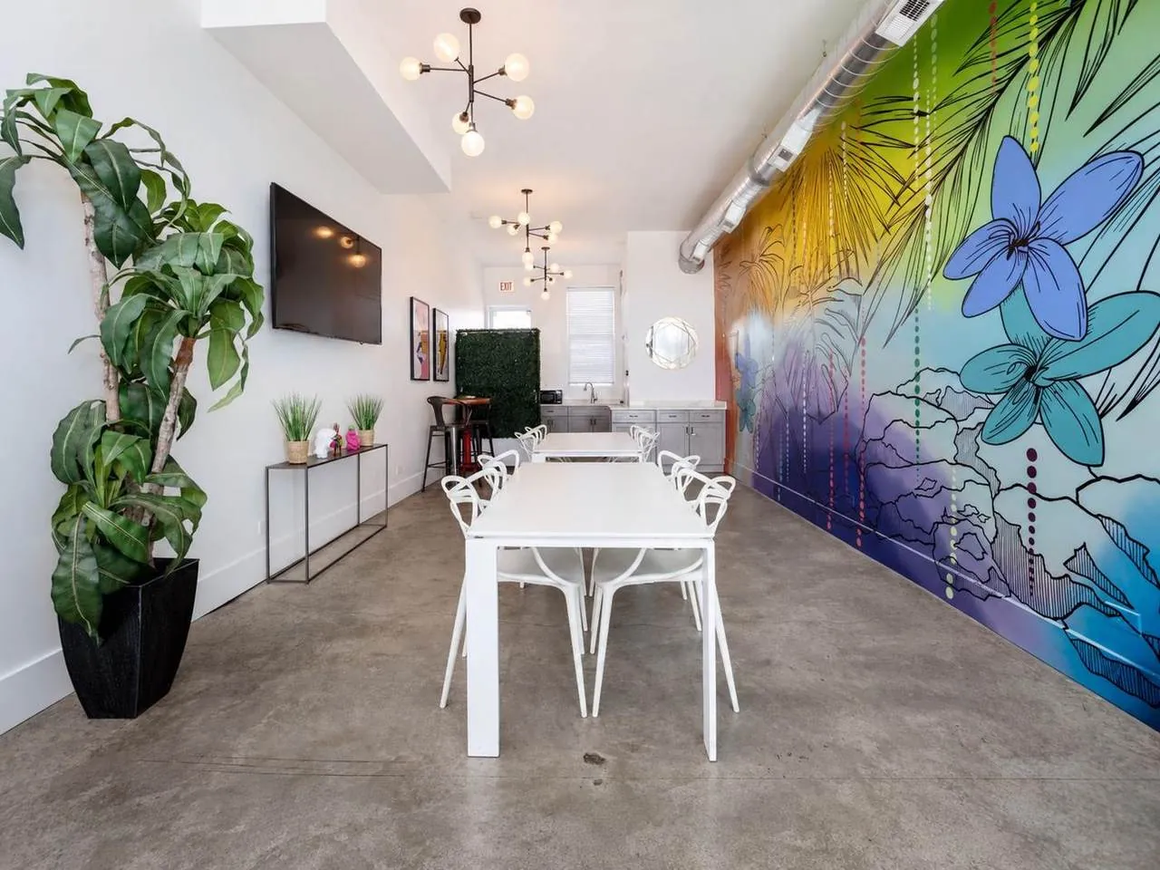 Nala’s Party Room main room with white dining tables beside the tropical mural