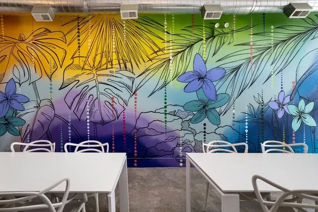 White tables and chairs by the tropical mural at Nala’s Party Room in Irving Park